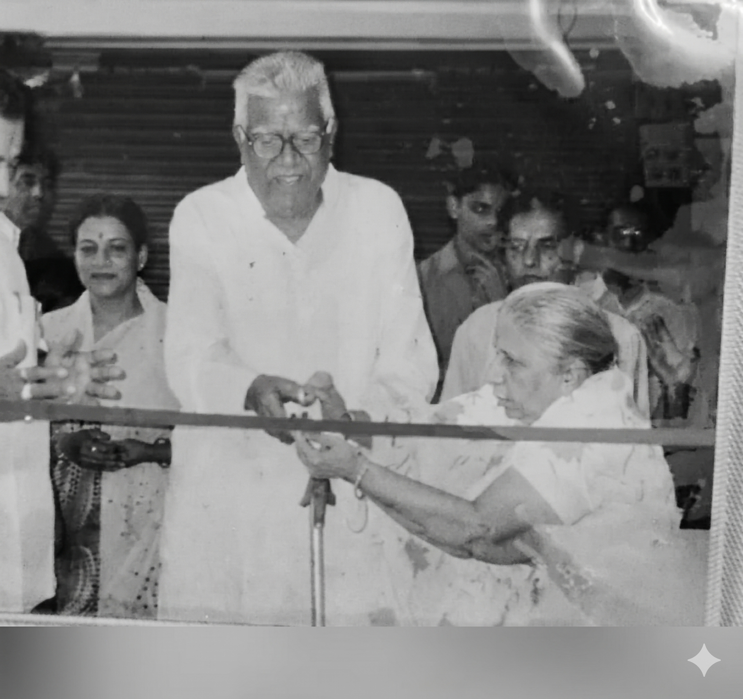 Black and white photograph of a man and woman cutting a ribbon together, with onlookers in the background.