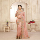 Woman in a traditional pink saree with intricate designs in an ornate room.