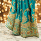 Close-up of a teal embroidered fabric with gold and multicolor patterns on a stand.